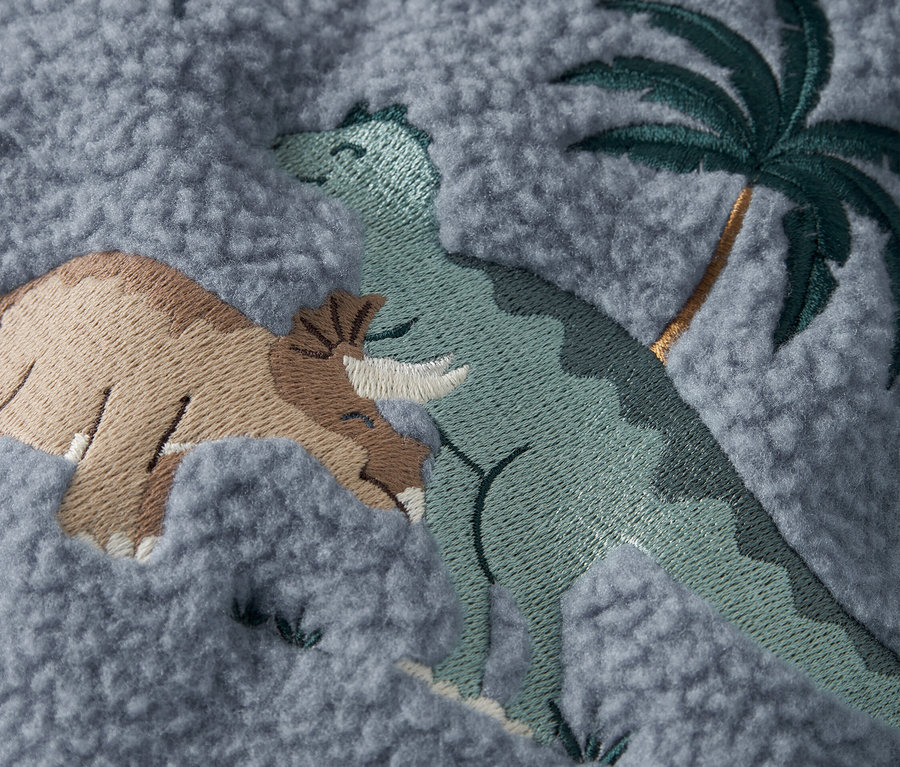 Zbliżenie szarej tkaniny z haftowanymi dinozaurami i palmą.