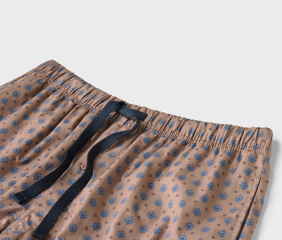 Zbliżenie na beżowe spodnie w niebieskie kwiaty ze sznurkiem w kolorze granatowym.