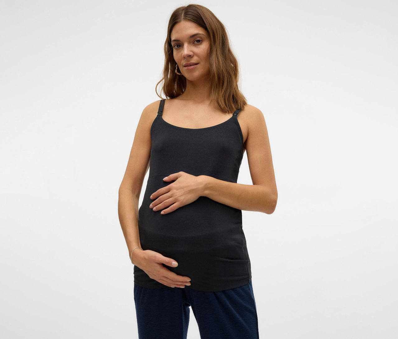 Kobieta w ciąży trzyma ręce na brzuchu, ma na sobie koszulkę na ramiączkach „MLKERRIE” firmy MAMALICIOUS.