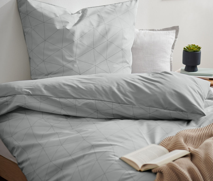 Szara pościel COOLMAX® z geometrycznym wzorem na łóżku z otwartą książką i beżowym kocem.