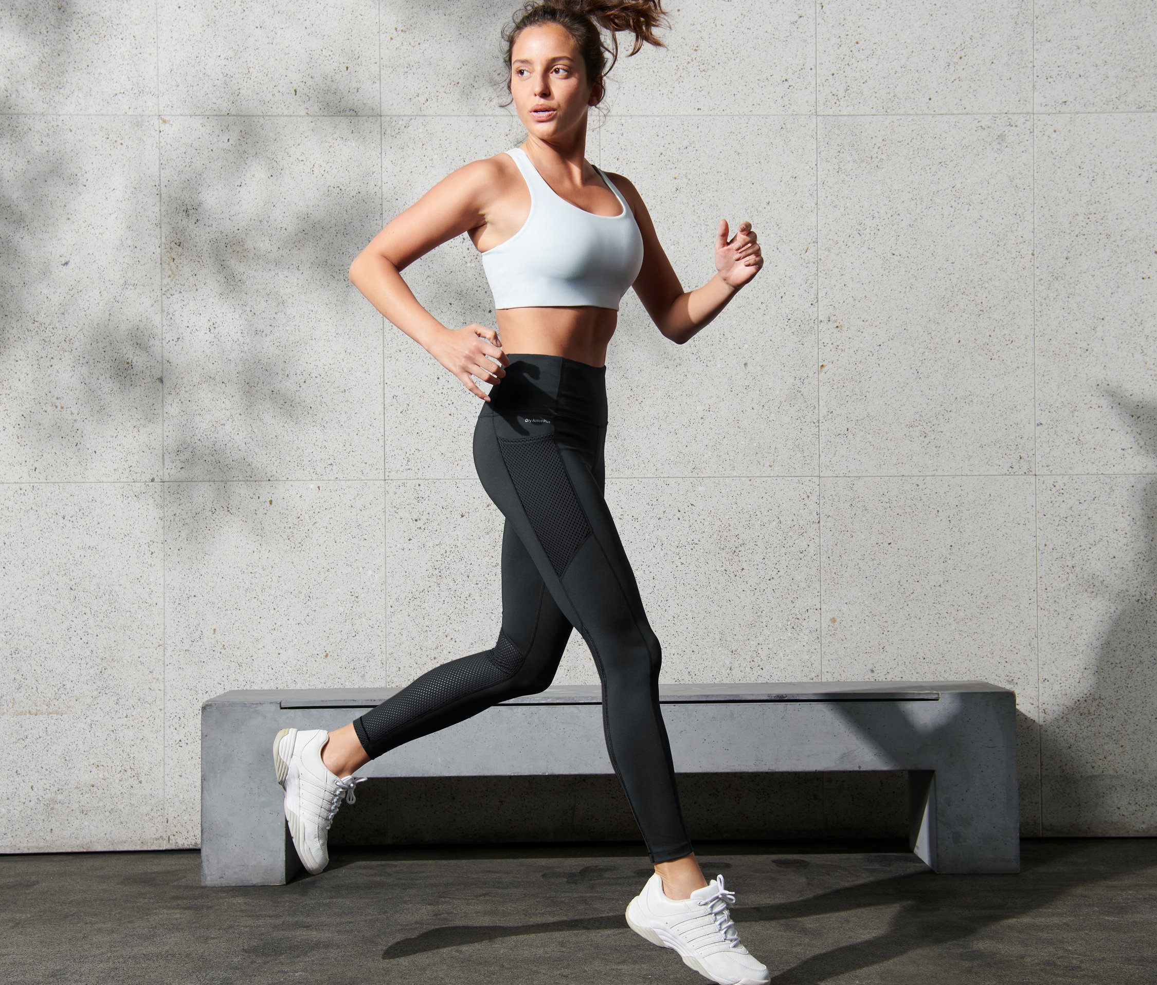 Kobieta w białym sportowym biustonoszu i sportowych legginsach z siateczką biegnie.