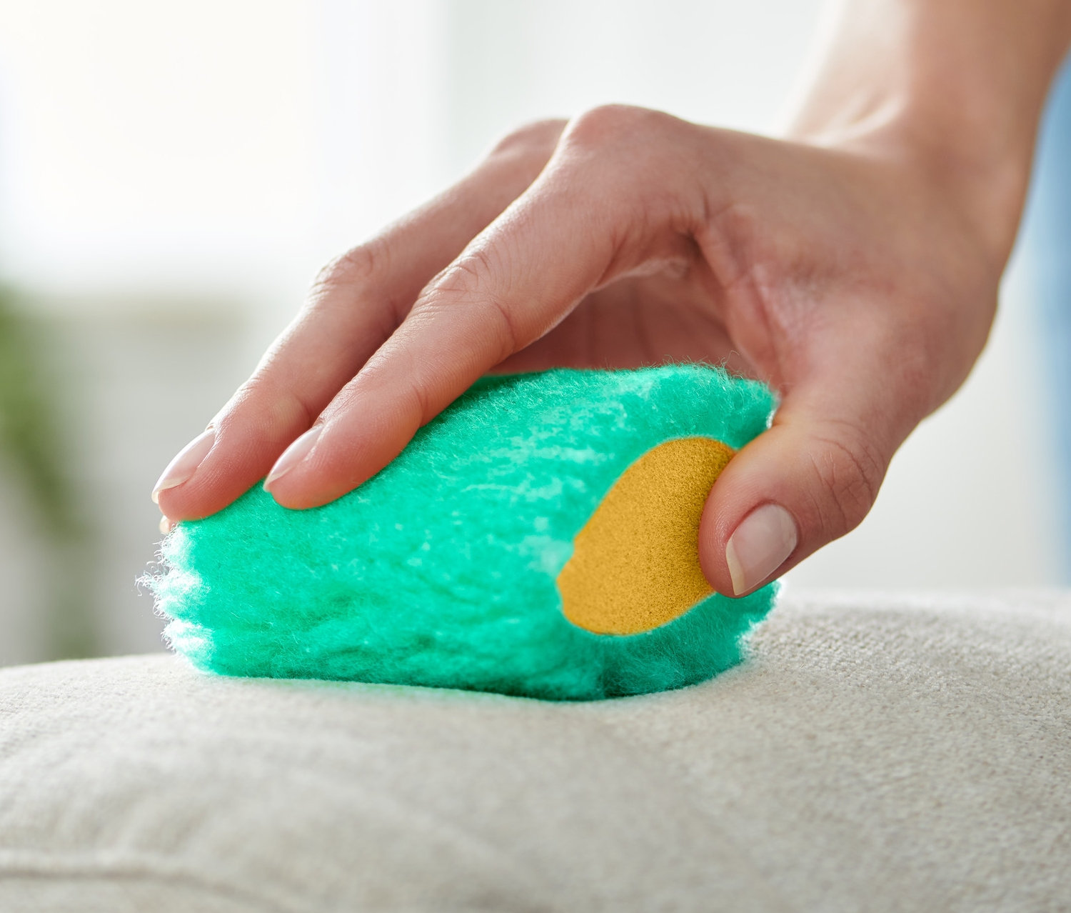 Ręka czyści beżową poduszkę zielonymi magicznymi gąbkami do usuwania plam, 2 sztuki.