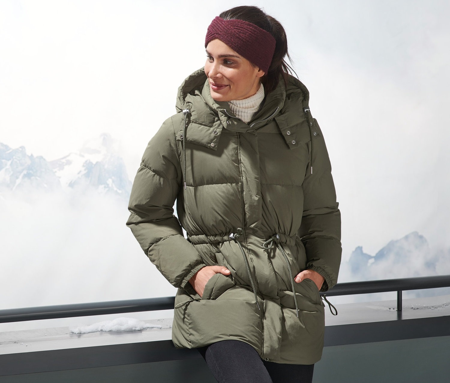 Kobieta w kurtce puchowej stoi na zewnątrz z górami w tle.