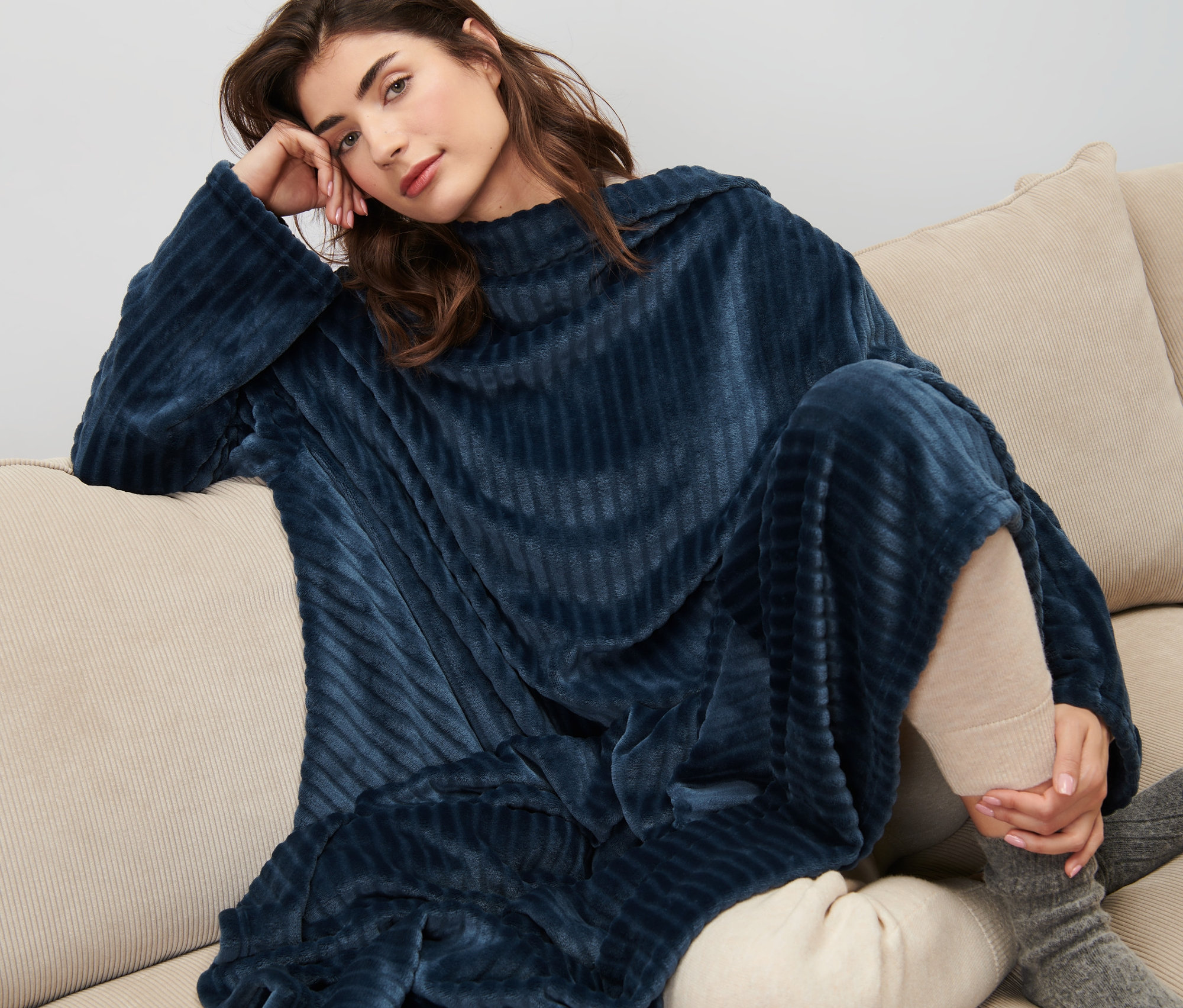 Kobieta siedzi na kanapie w kocu z rękawami.