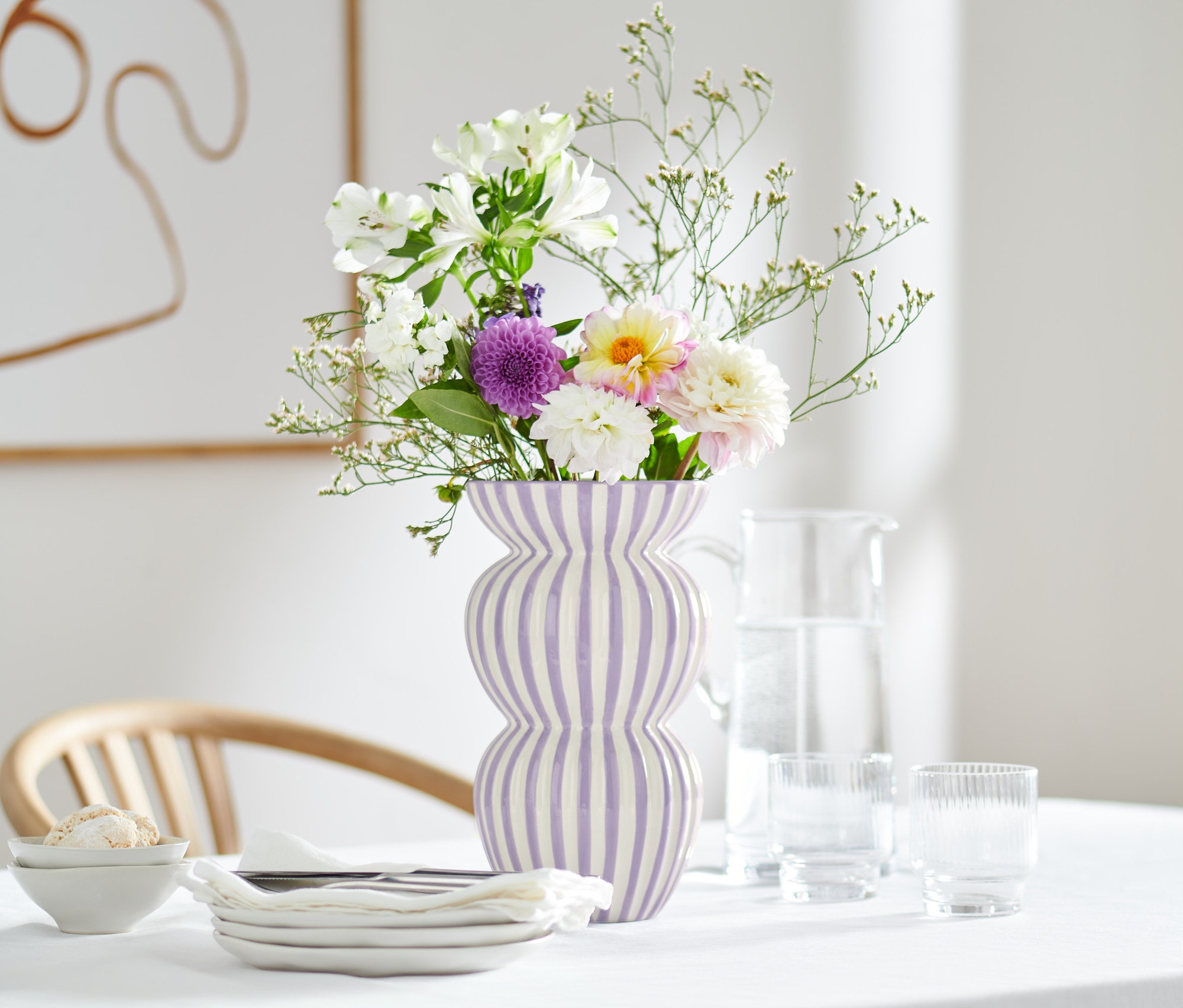 Kwiaty w dużym wazonie w fioletowe paski na stole z kwiecistym obrusem.