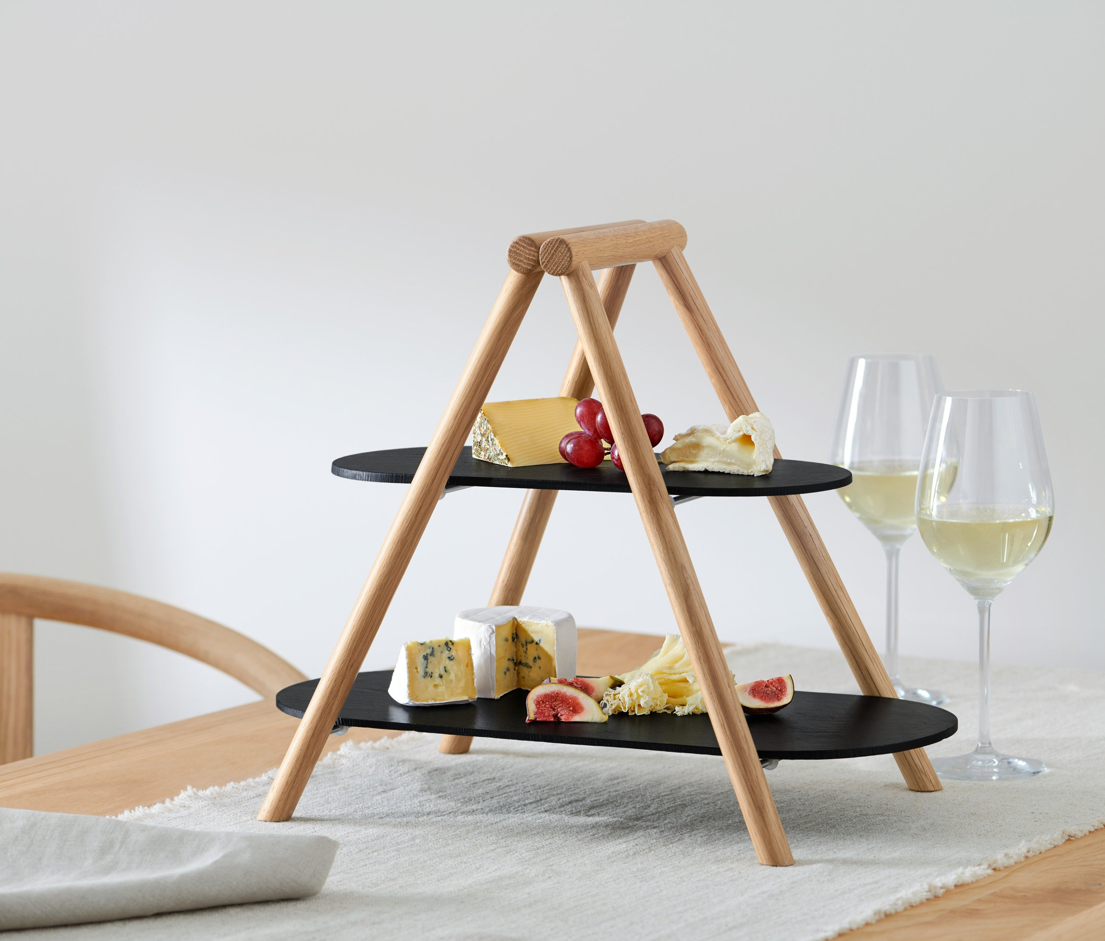 Dwupoziomowa patera piętrowa z serami, winogronami i figami stoi na stole obok kieliszków do wina.