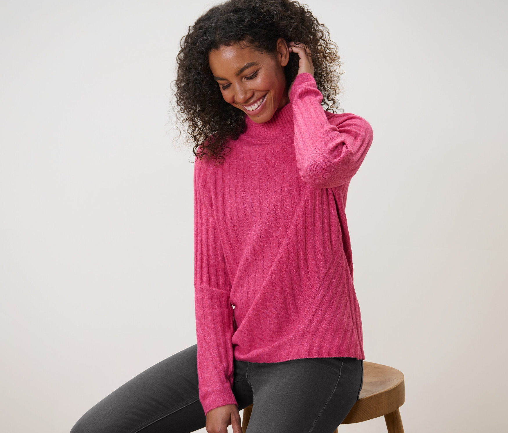 Kobieta siedzi na stołku i ma na sobie prążkowany sweter z dzianiny ze stójką.