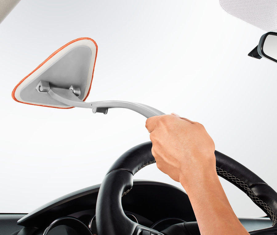 Ręka trzyma myjkę do szyb samochodowych i czyści przednią szybę samochodu.