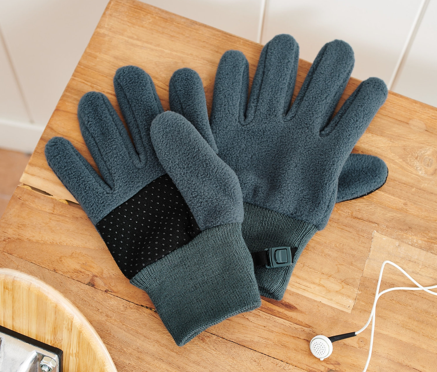 Dwie pary rękawiczek z polaru dla dzieci leżą na drewnianej ławce obok deskorolki i słuchawek.