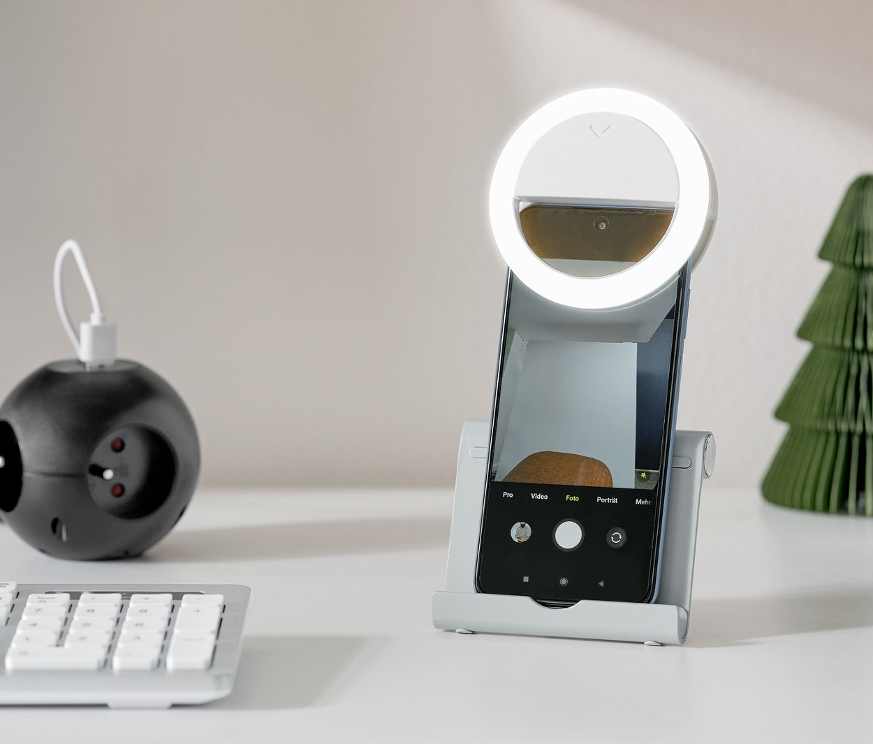 Srebrny stojak na smartfon lub tablet trzyma smartfon z okrągłym światłem na białym stole.