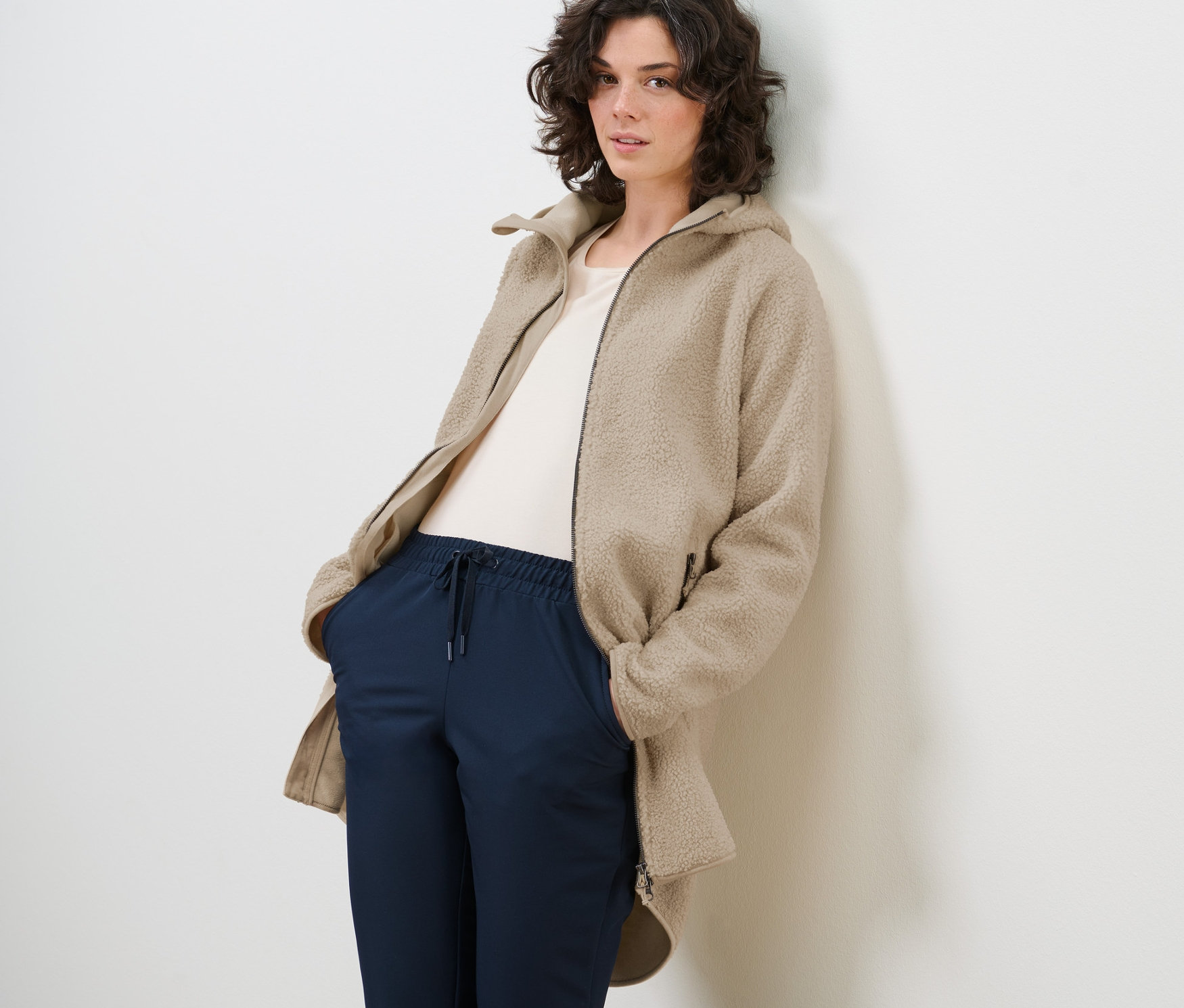 Kobieta pozuje w płaszczu z pluszowego polaru, białym t-shircie i niebieskich spodniach.