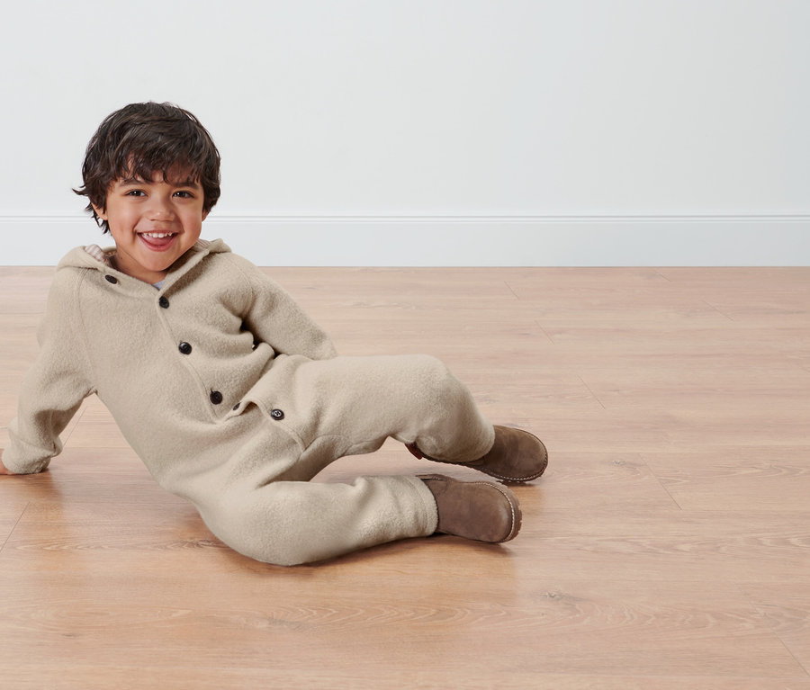 Chłopiec leży na podłodze w kombinezonie z wełny merino.