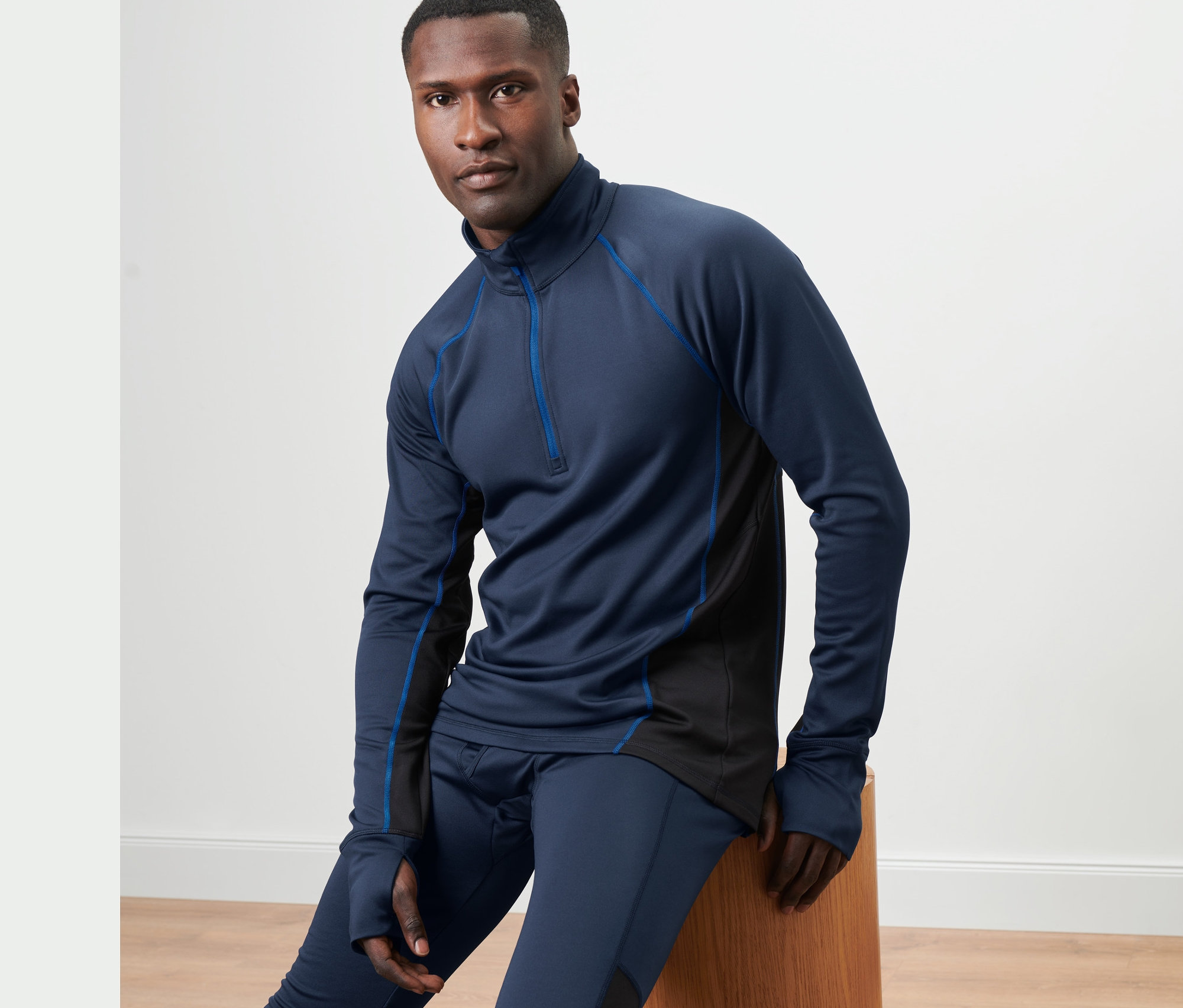 Mężczyzna siedzi na drewnianym stołku, ubrany w niebieską termoaktywną bluzę funkcyjną.