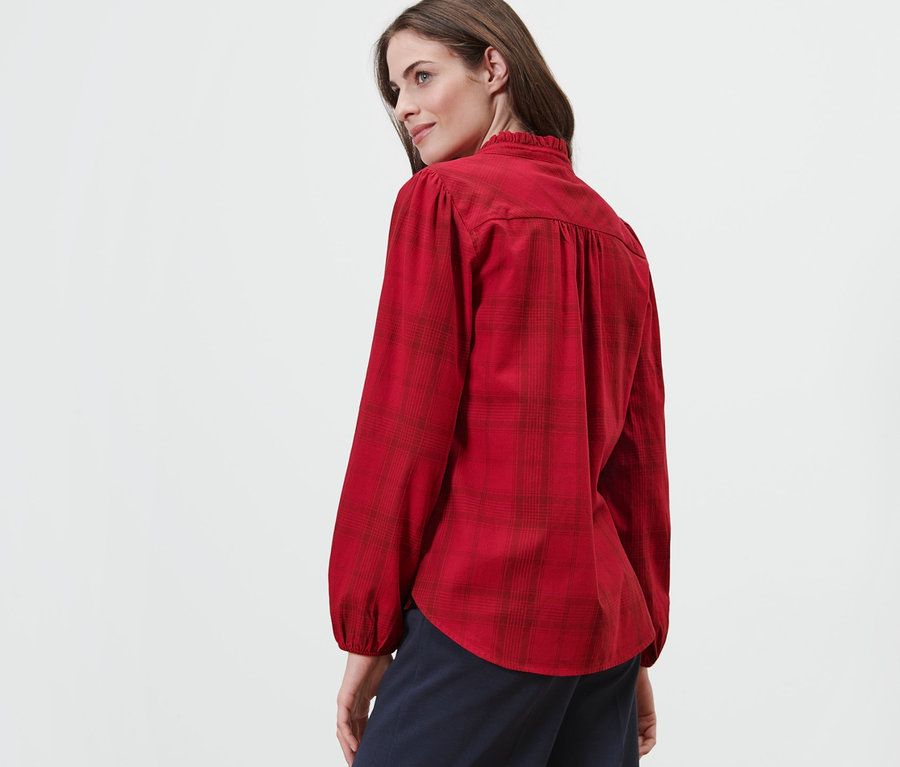 Kobieta patrzy przez ramię, ubrana w bluzkę w kratkę z wiązaniem.