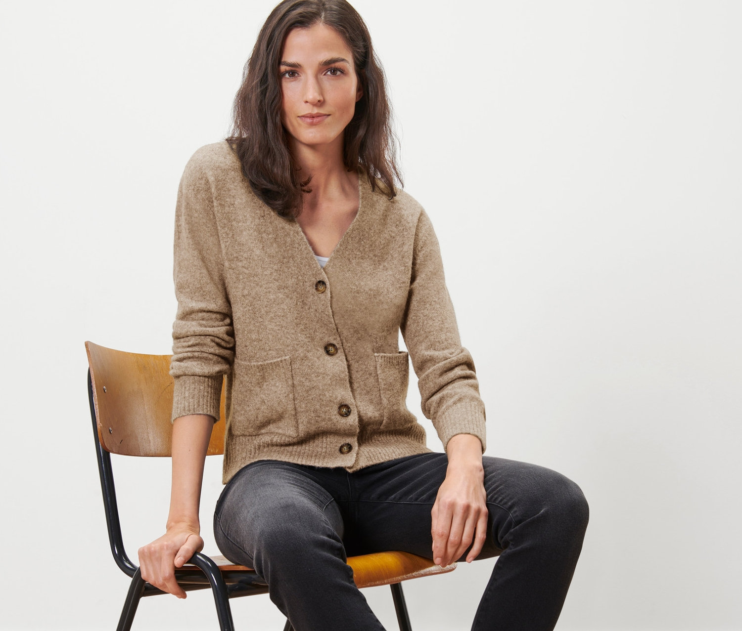 Kobieta siedzi na krześle i ma na sobie rozpinany sweter z zawartością wełny.