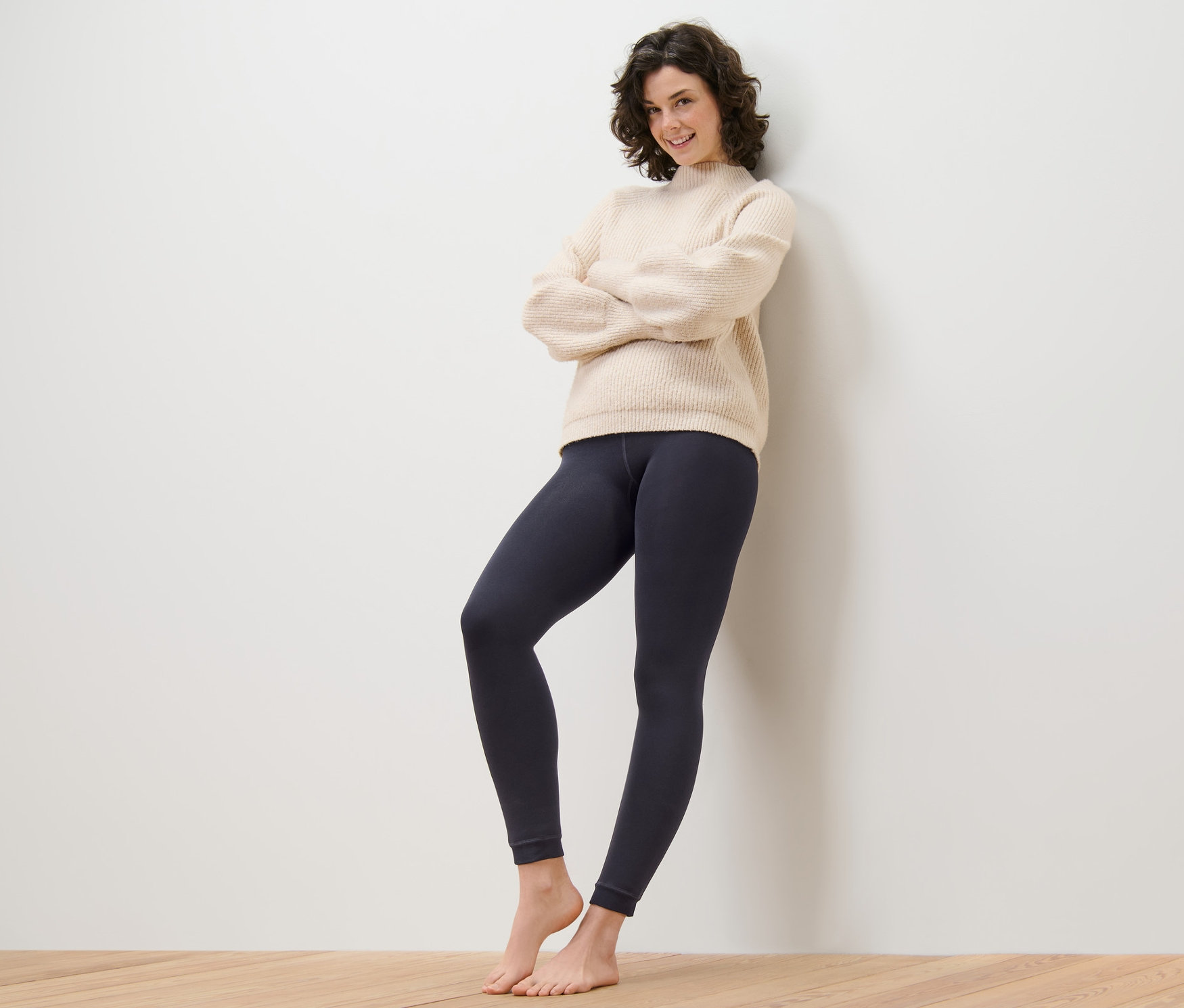 Kobieta stoi oparta o ścianę ze skrzyżowanymi ramionami, ubrana w legginsy z podszewką.