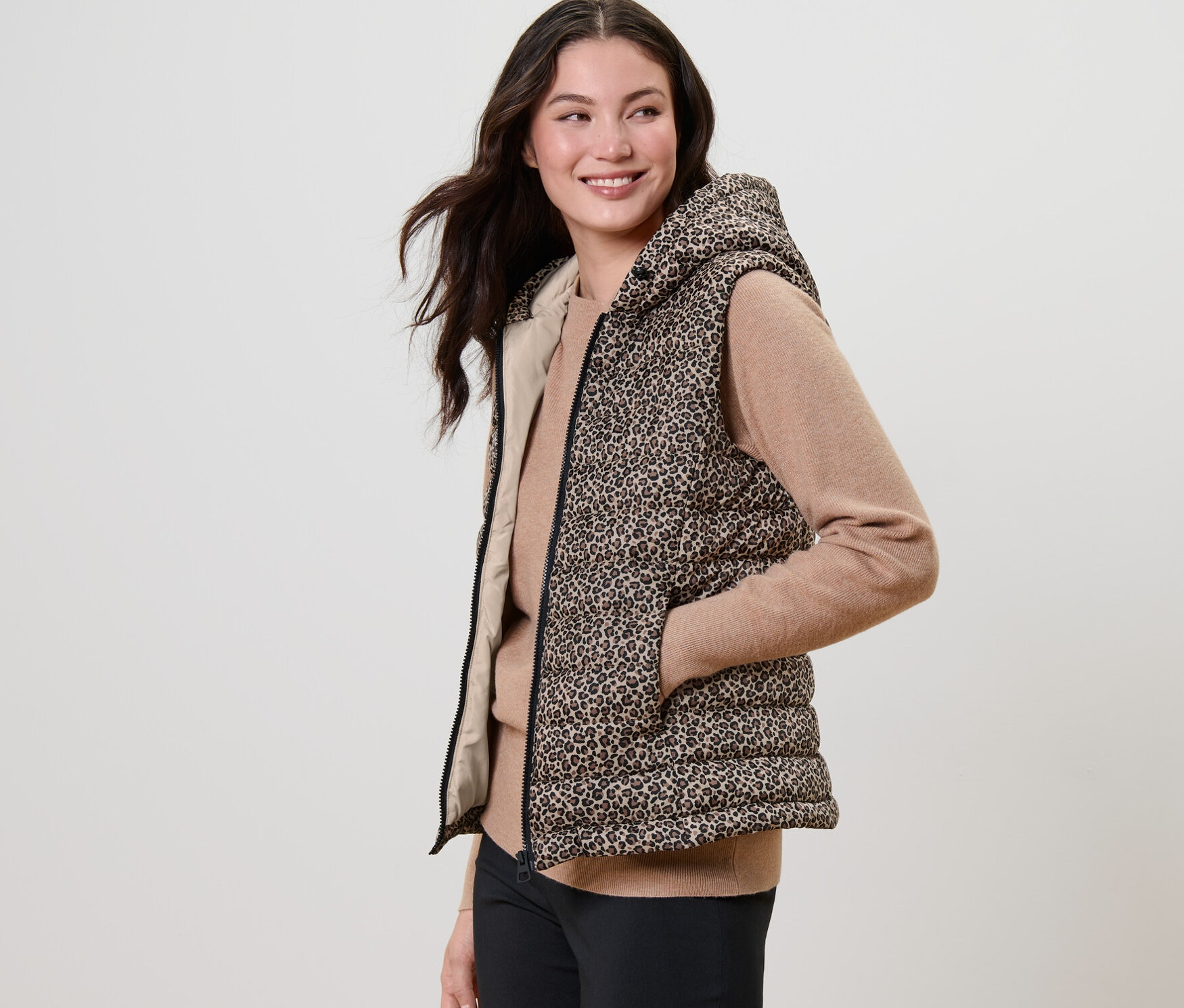 Kobieta pozuje w wzorzystej pikowanej kamizelce z kapturem.
