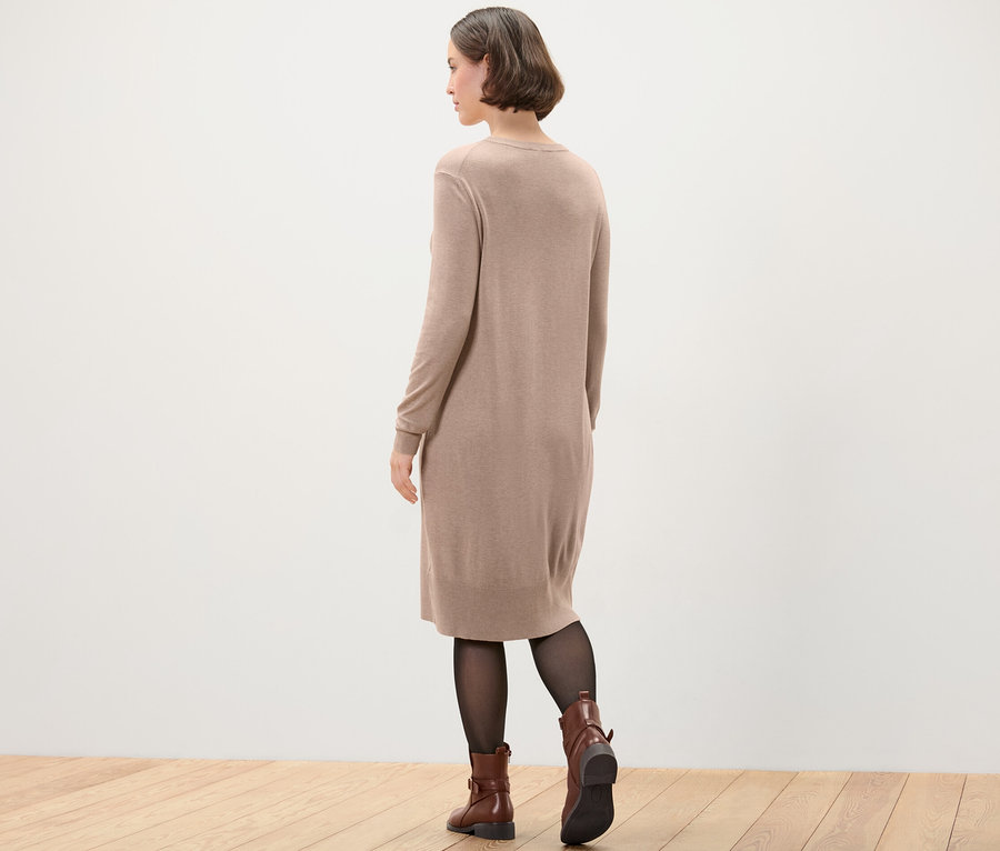 Kobieta w sukience z cienkiej dzianiny, czarnych rajstopach i brązowych butach.