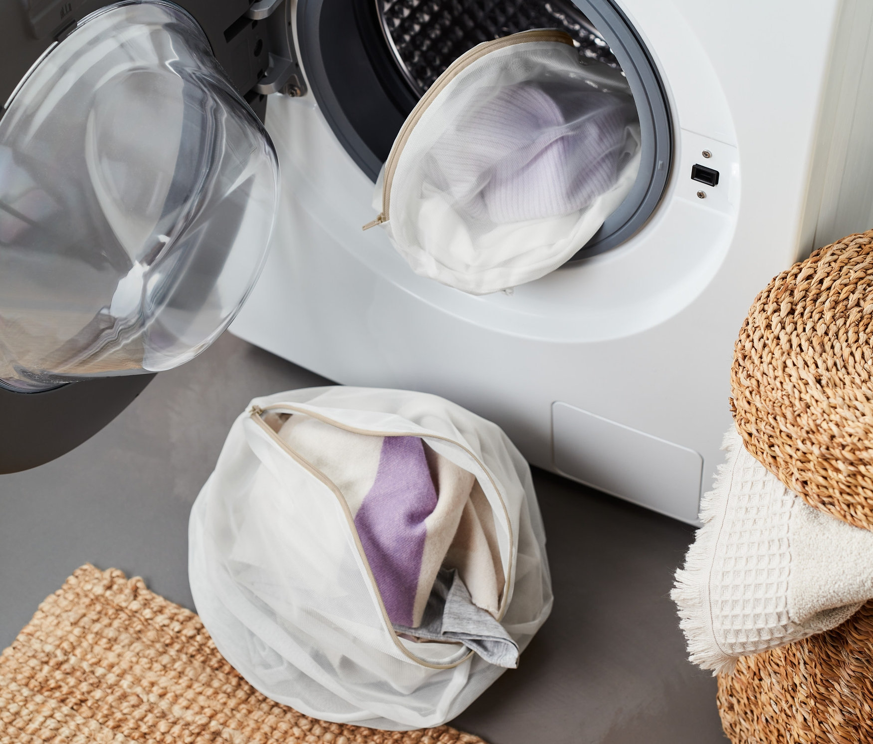 Dwie woreczki do prania, jedna w pralce, a druga na podłodze obok wycieraczki.