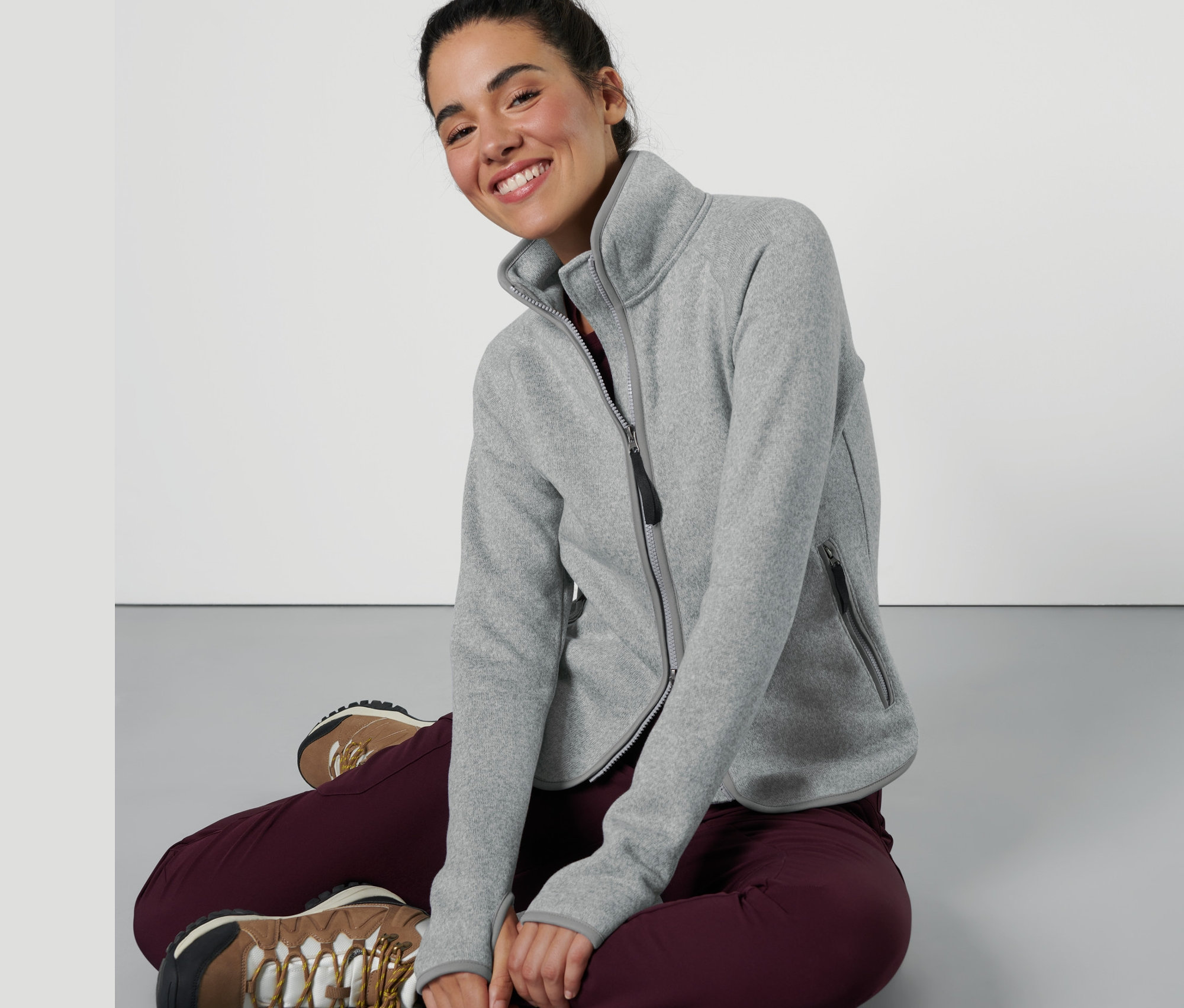 Kobieta siedzi i ma na sobie jasnoszarą rozpinaną bluzę z dzianiny polarowej.