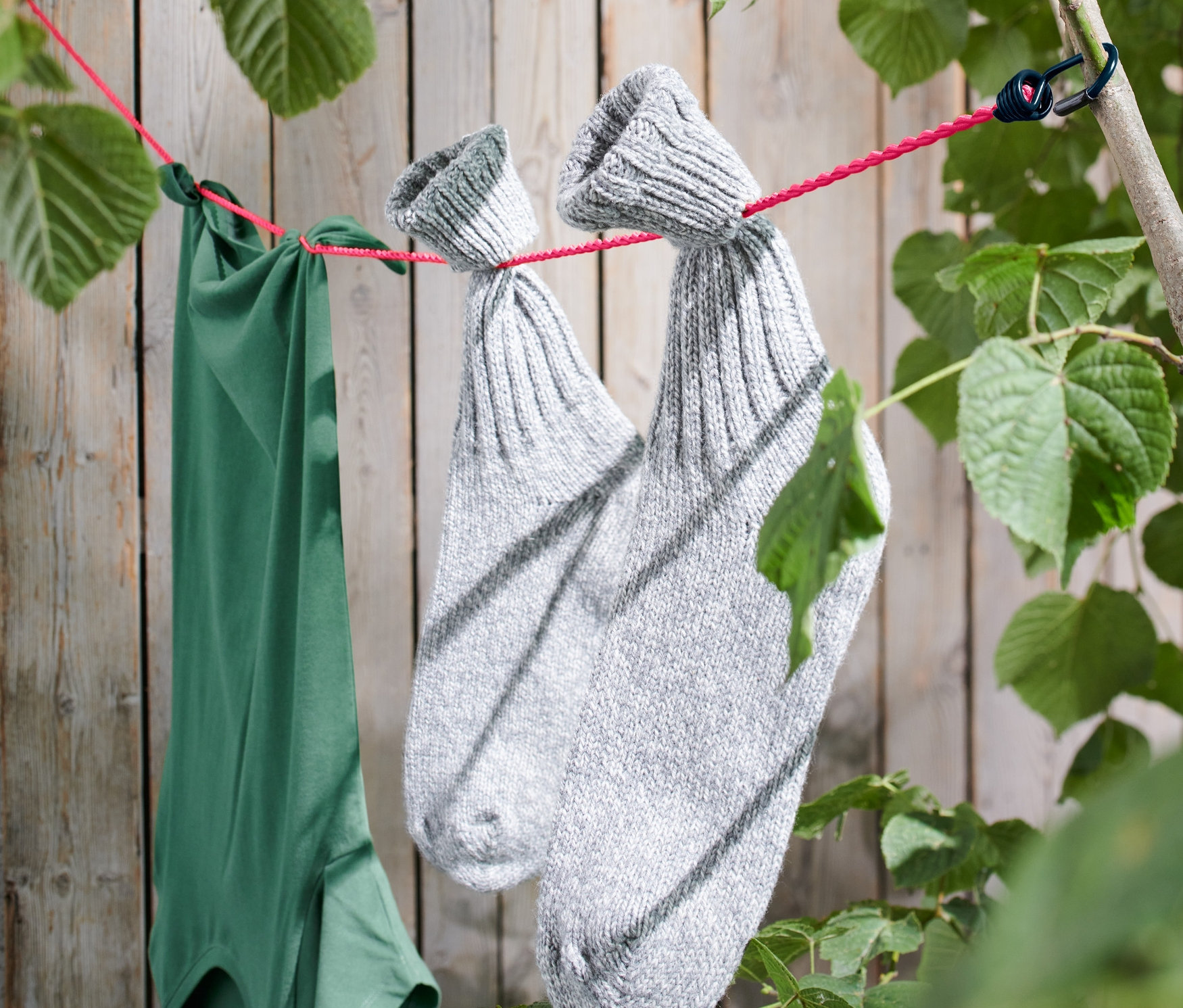 Zielona koszulka i para szarych wełnianych skarpet wiszą na kempingowej lince na pranie przymocowanej do gałęzi drzewa.