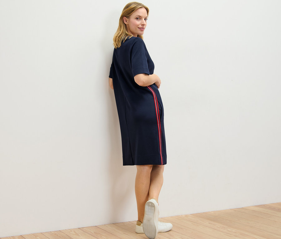 Kobieta spogląda przez ramię i pozuje w sukience dresowej z lampasami.