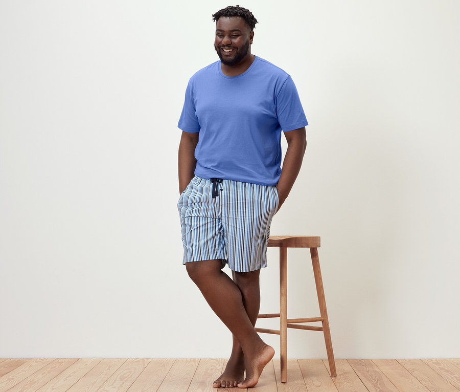 Mężczyzna opiera się o stołek, ubrany w piżamę z krótkimi spodenkami.