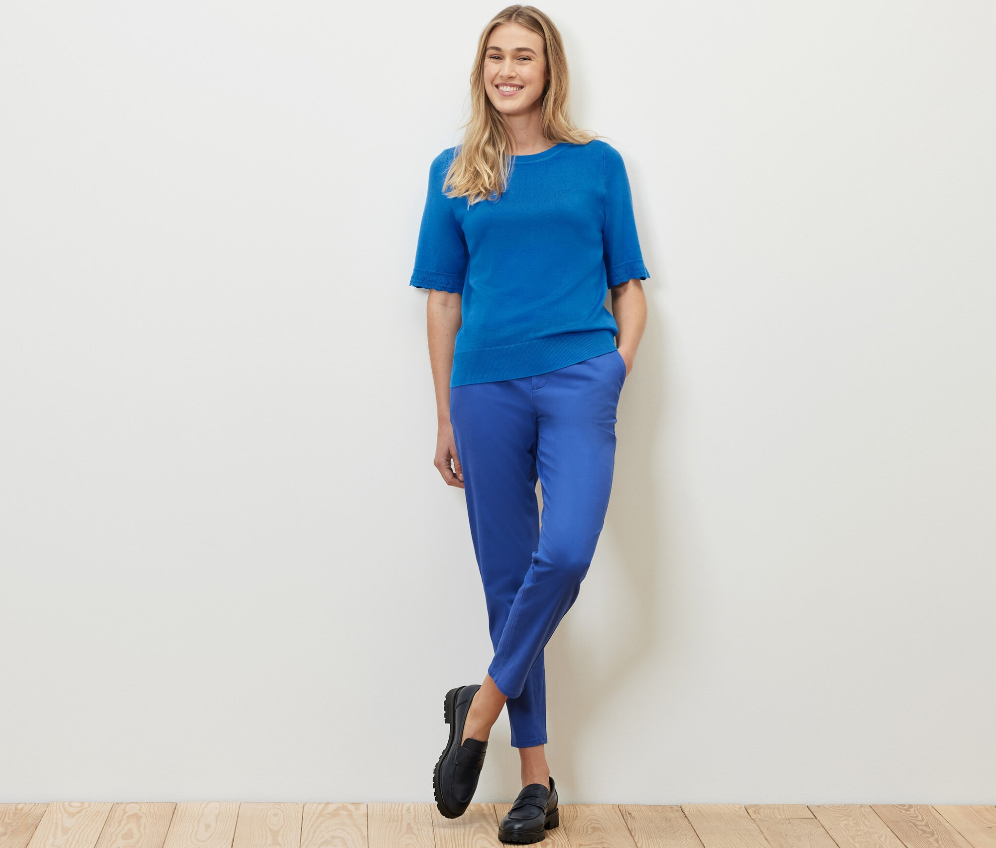 Kobieta pozuje w kobaltowym cienkim swetrze i niebieskich spodniach.