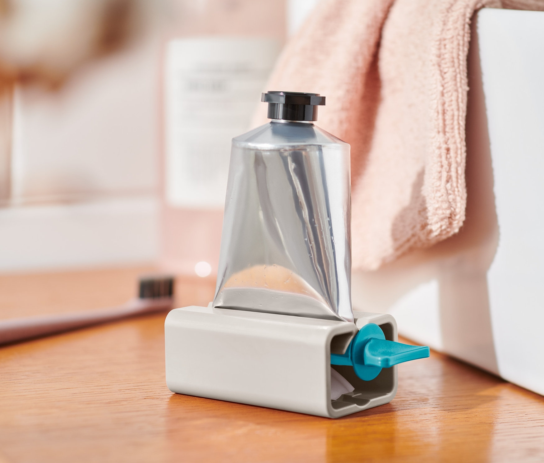 Srebrna tuba w szarym wyciskaczu do tubek na drewnianej półce.