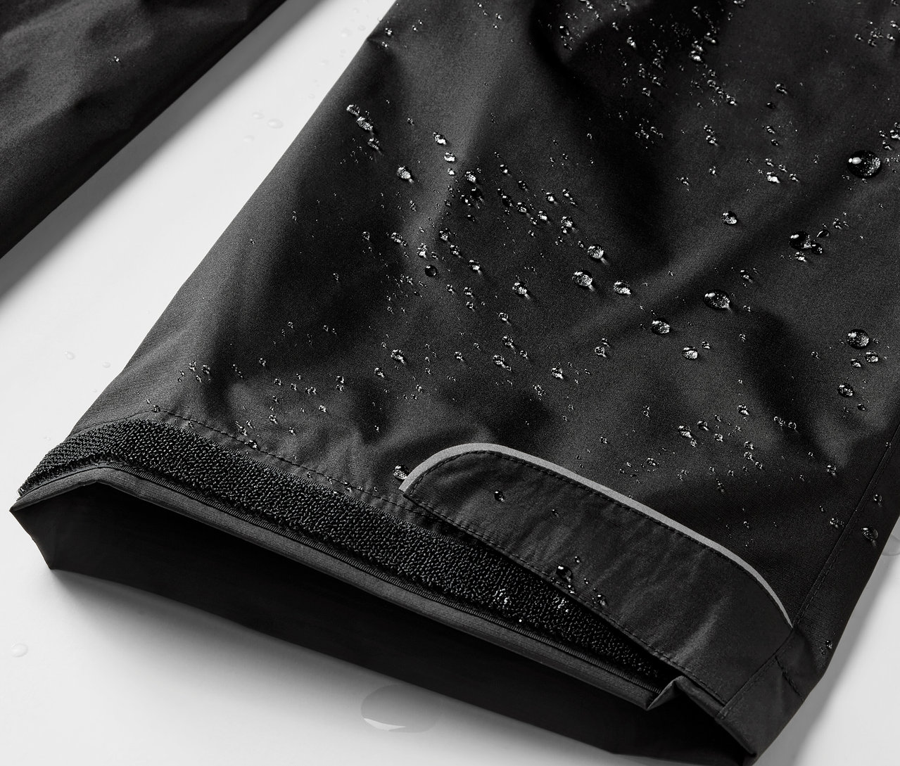 Zbliżenie na czarne spodnie przeciwdeszczowe z kroplami wody.