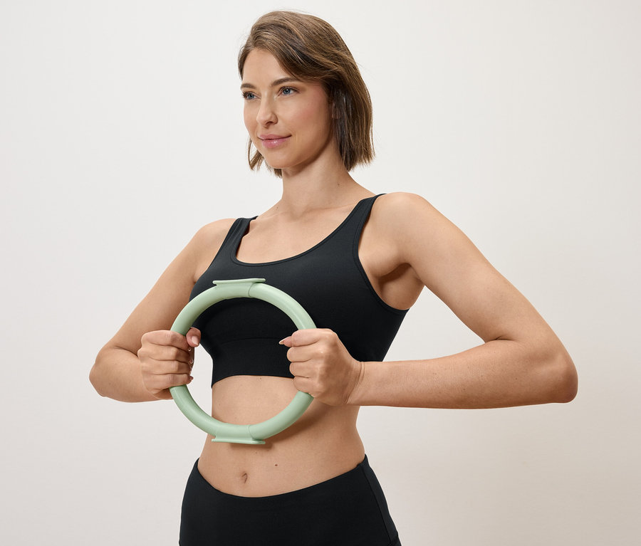 Kobieta trzyma jasnozielone kółko do ćwiczeń przed sobą, ubrana w czarny sportowy top i legginsy.