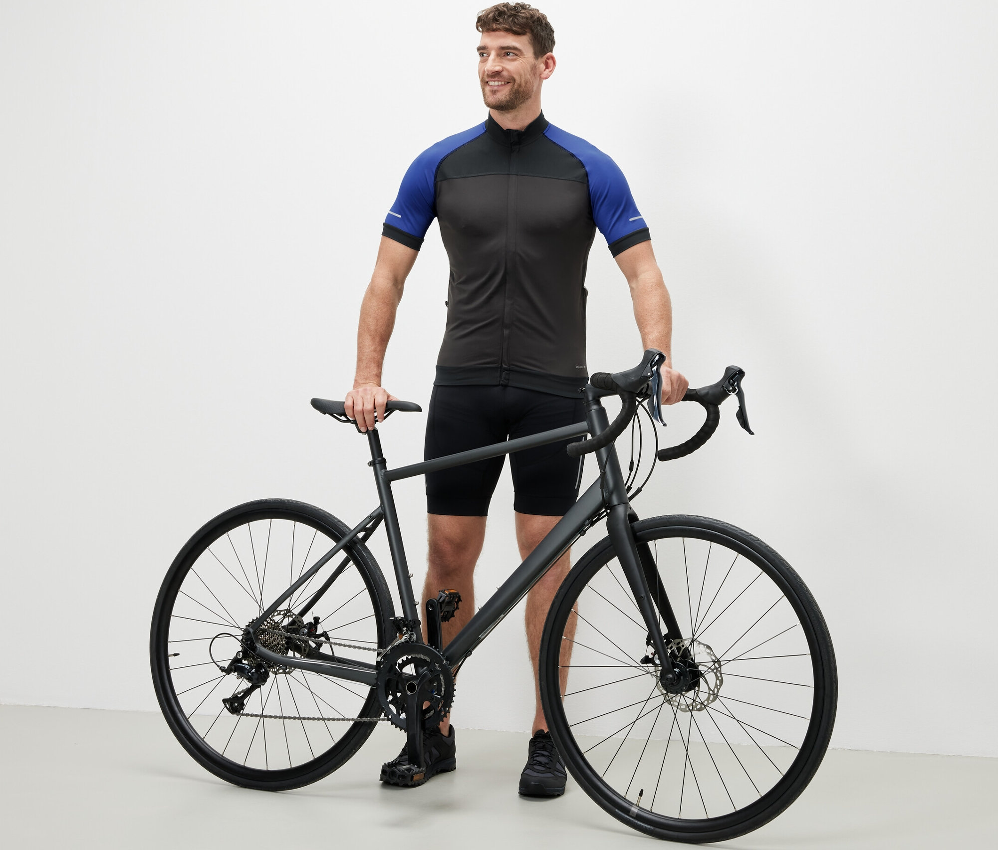 Mężczyzna stoi obok roweru w antracytowej koszulce rowerowej.