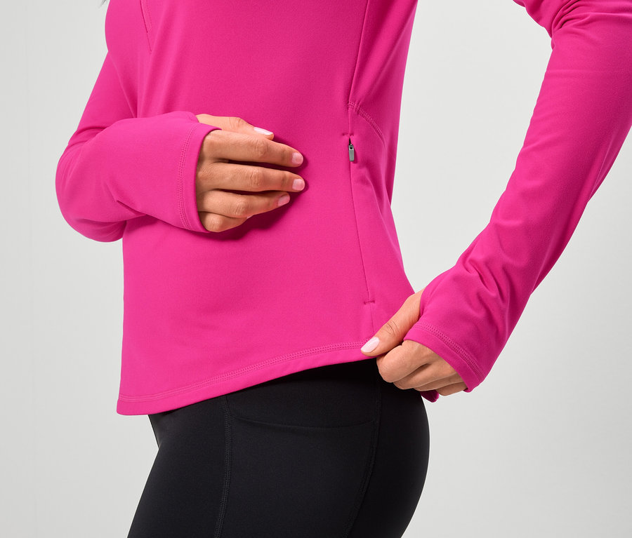 Kobieta ma na sobie różową bluzkę z długim rękawem i czarne legginsy.