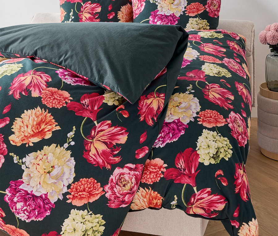 Pościel w kwiaty na łóżku z ciemnozielonym kocem.
