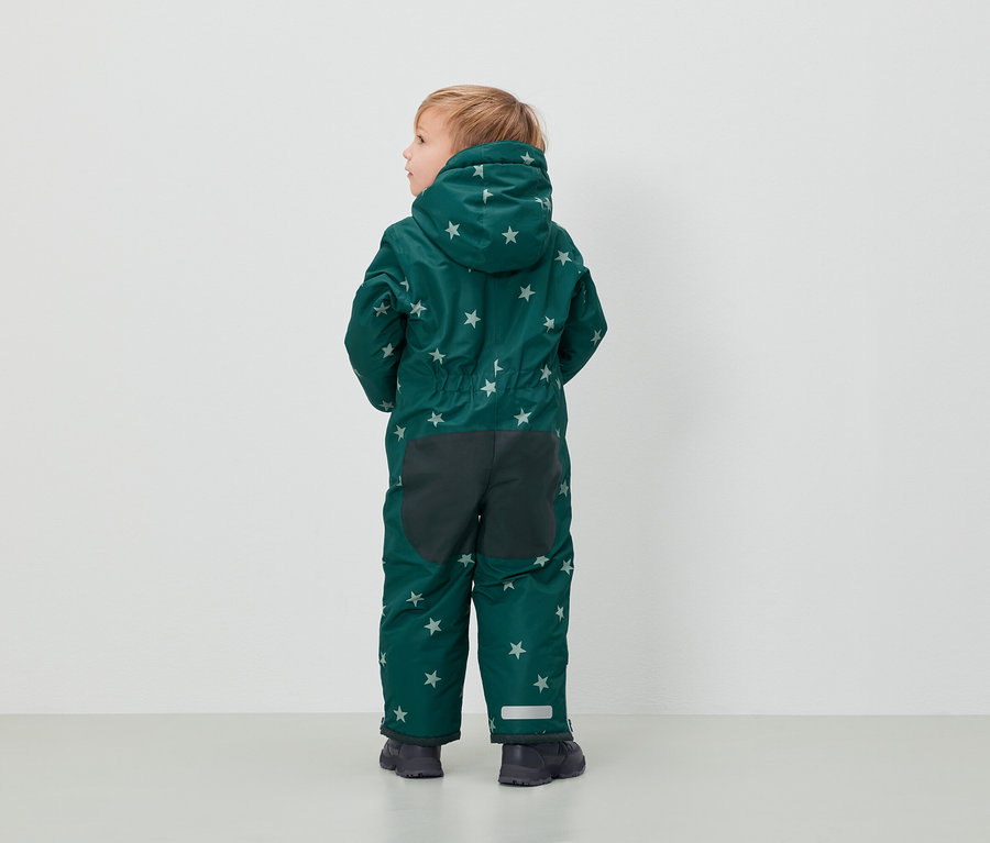 Chłopiec w zielonym kombinezonie w gwiazdy stoi tyłem do aparatu.