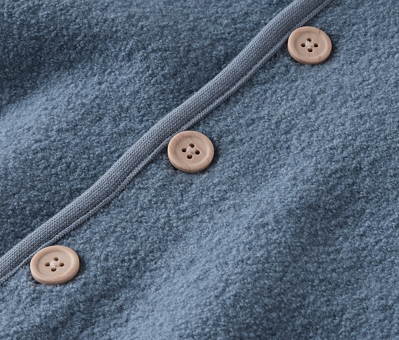 Zbliżenie na niebieski sweter z brązowymi guzikami.
