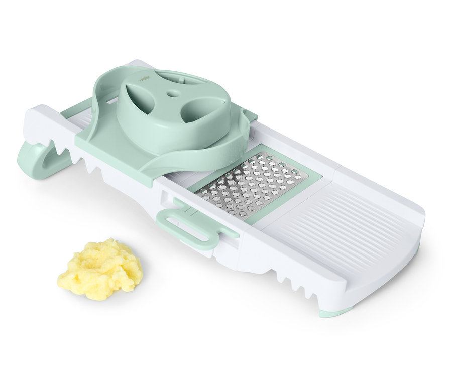 Biała i zielona krajalnica mandolina z stertą pokrojonych warzyw.