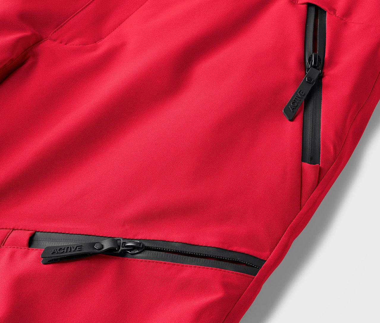 Szczegół czerwonych spodni z czarnymi zamkami błyskawicznymi przy kieszeniach.