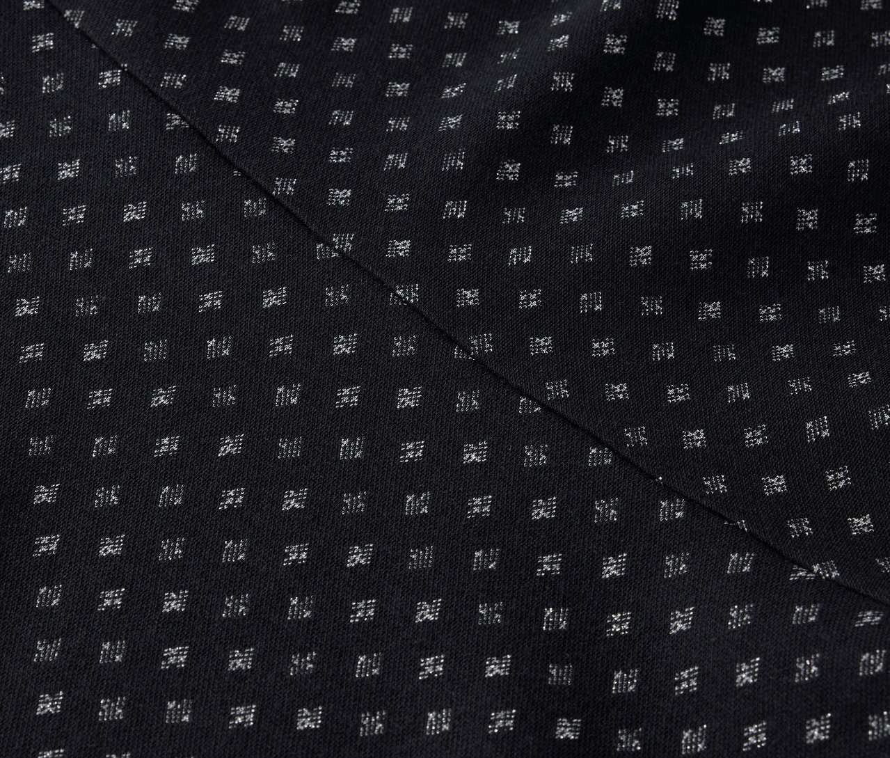 Zbliżenie czarnej tkaniny z regularnym wzorem małych białych kwadratów i ukośnym szwem.
