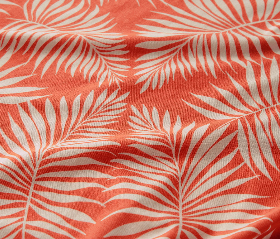 Zbliżenie na wzorzystą bluzkę z białym motywem liści palmowych na koralowym tle.