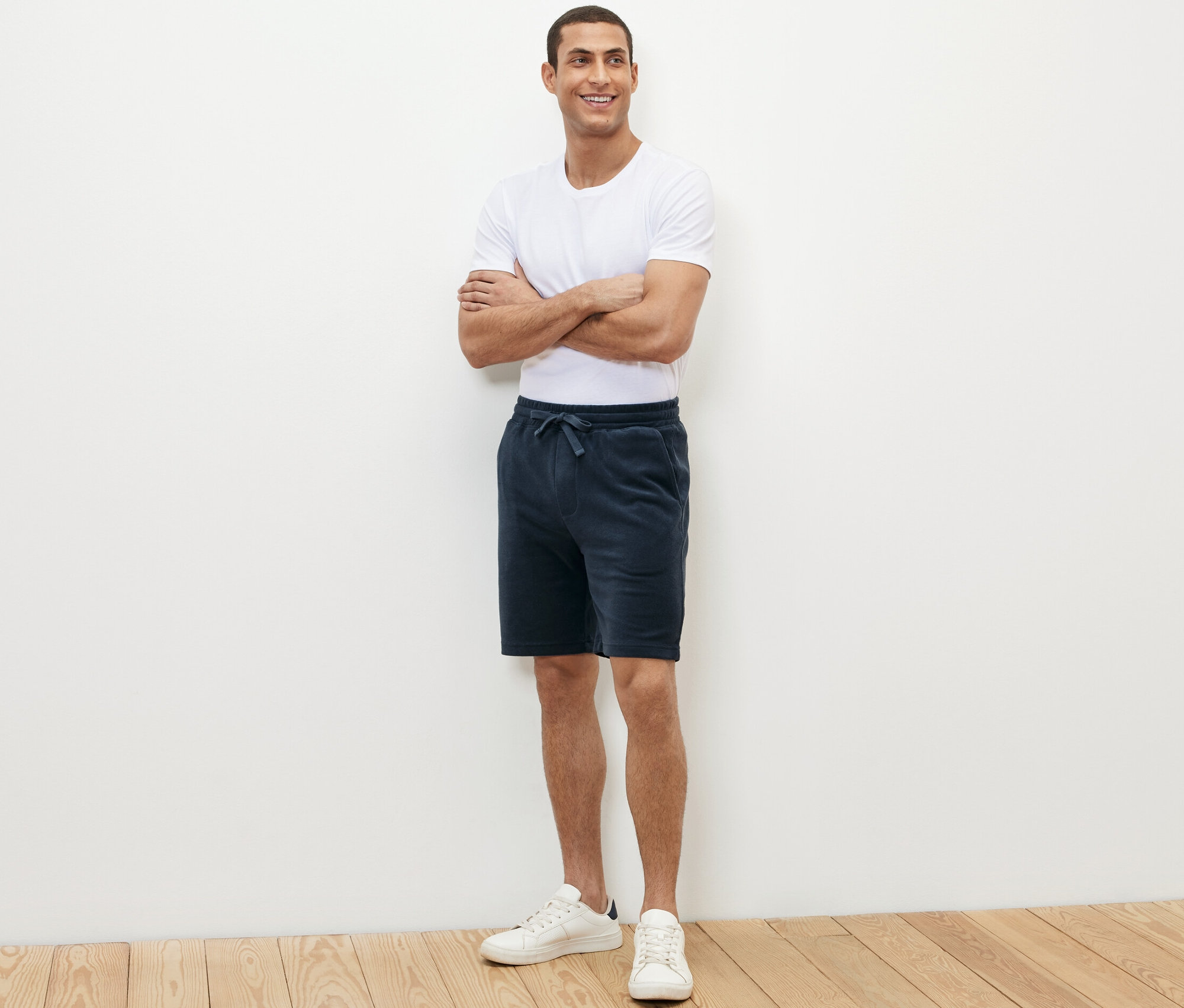 Mężczyzna stoi ze skrzyżowanymi ramionami, ubrany w granatowe szorty z tkaniny frotte.