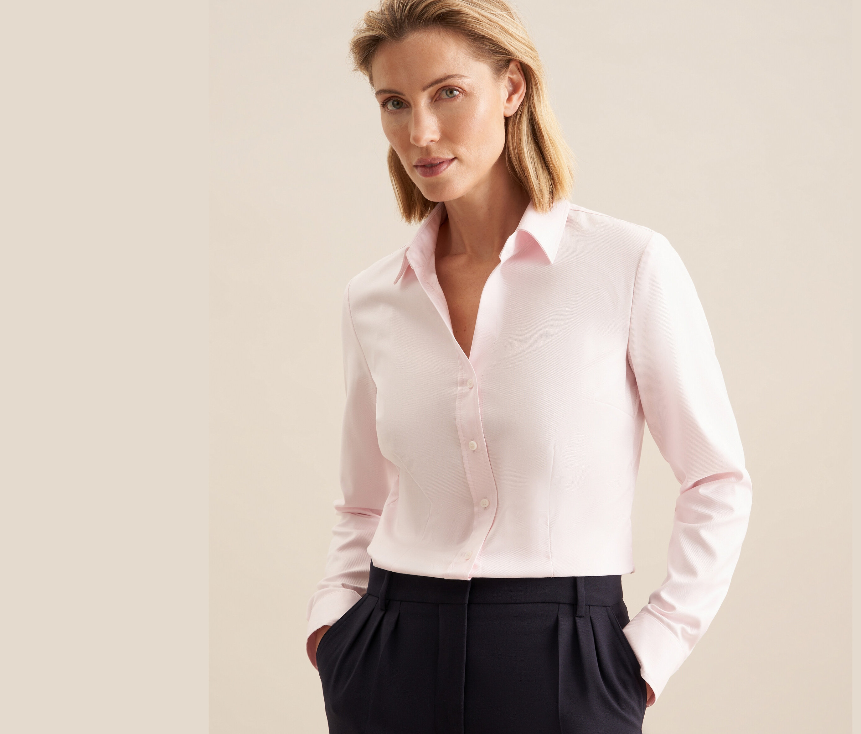 Kobieta ma na sobie różową koszulę z twillu Seidensticker i granatowe spodnie.