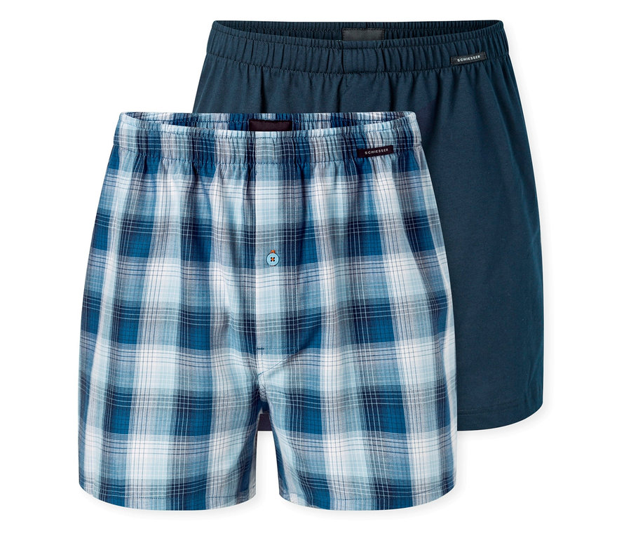 Dwie pary bokserek tkaninowych SCHIESSER. Jedna para jest niebiesko-biała w kratę z guzikiem, druga jest jednolicie ciemnoniebieska.