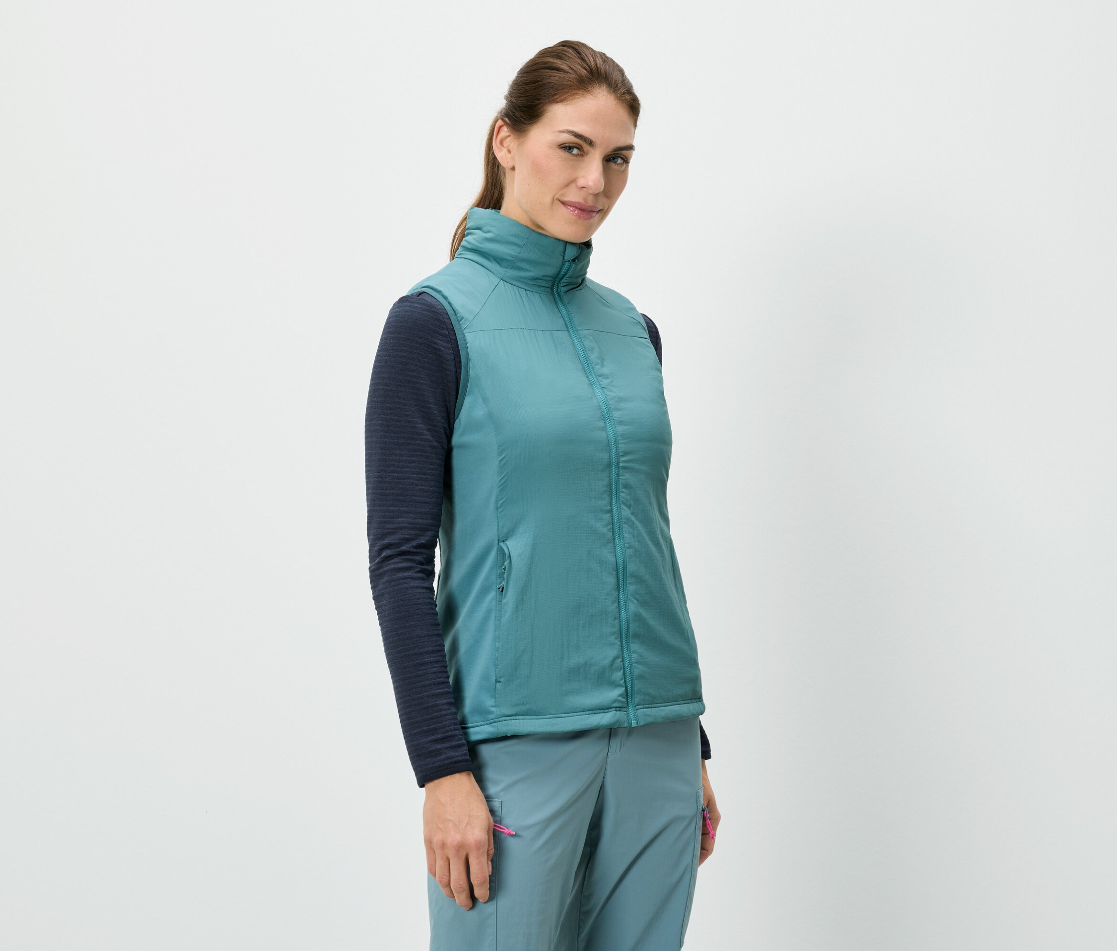 Kobieta stoi i ma na sobie niebieską kamizelkę nałożoną na koszulę z długimi rękawami, w połączeniu z niebieskimi spodniami.