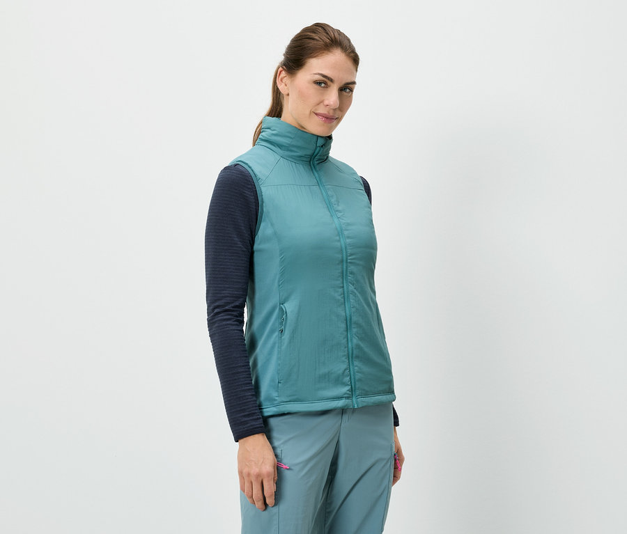 Kobieta stoi i ma na sobie niebieską kamizelkę nałożoną na koszulę z długimi rękawami, w połączeniu z niebieskimi spodniami.