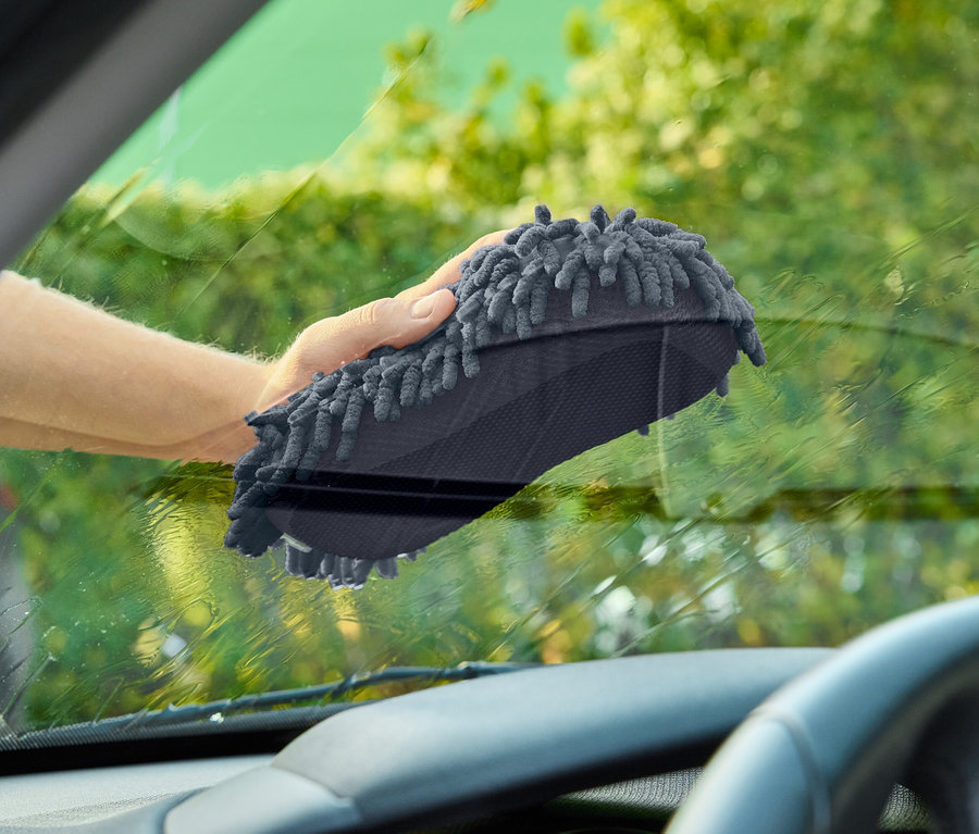 Ręka czyści szarą myjką przednią szybę samochodu.