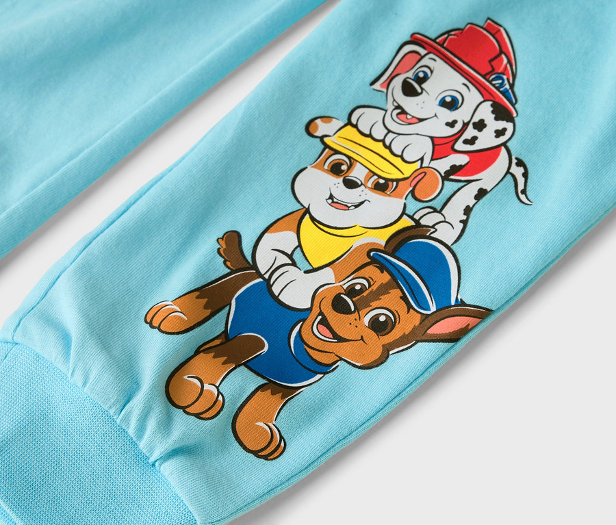 Zbliżenie jasnoniebieskiej nogawki spodni z postaciami z Psiego Patrolu: Marshallem, Rubblem i Chase'em.