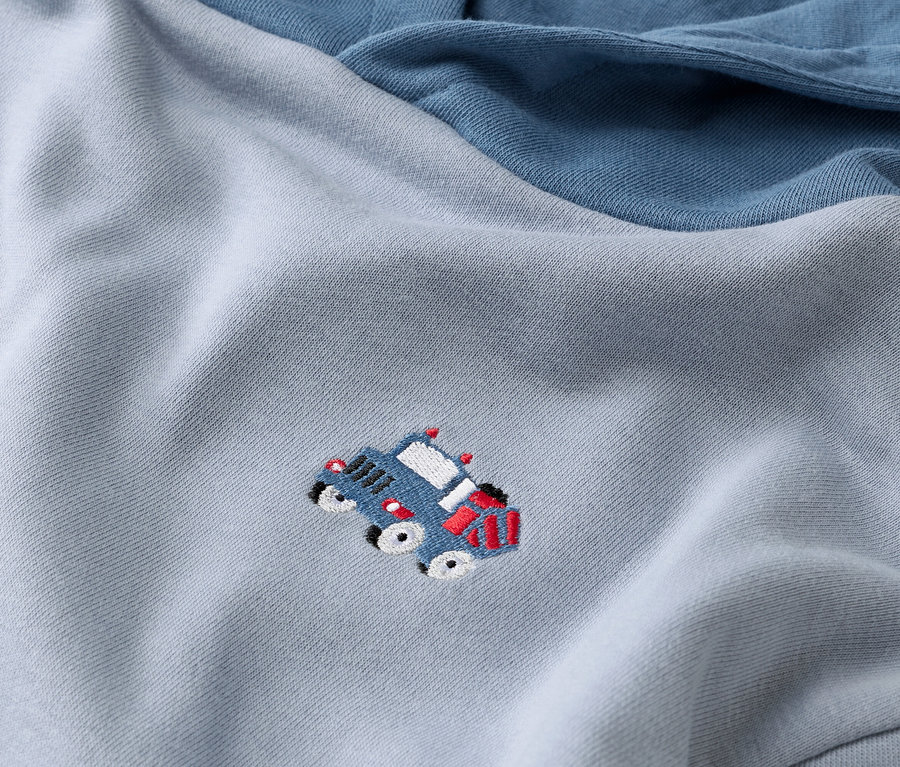 Zbliżenie jasnoniebieskiej bluzy z granatowym rękawem i aplikacją z niebieskiego samochodu.