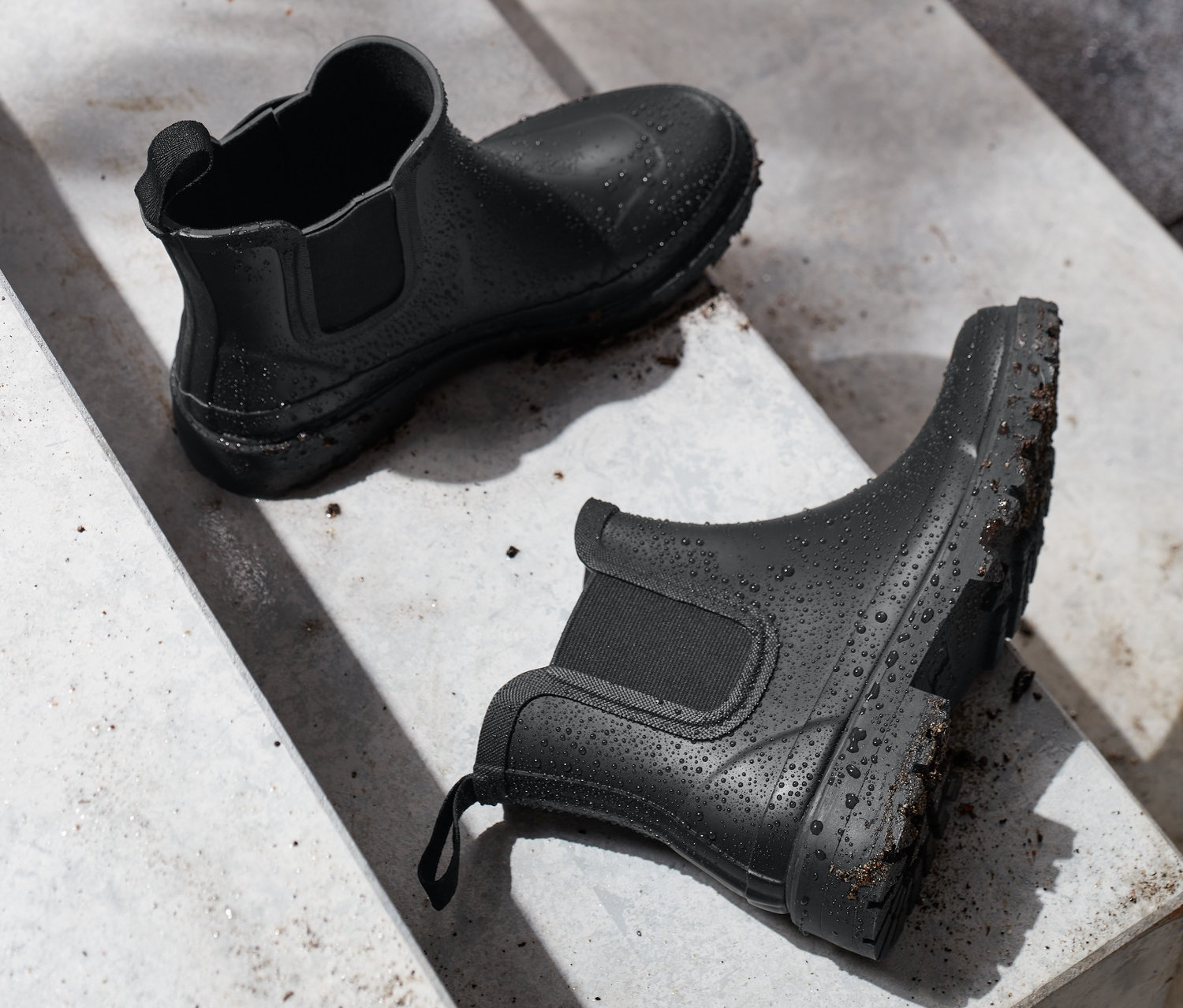 Dwa czarne krótkie kalosze leżą na betonowych schodach.