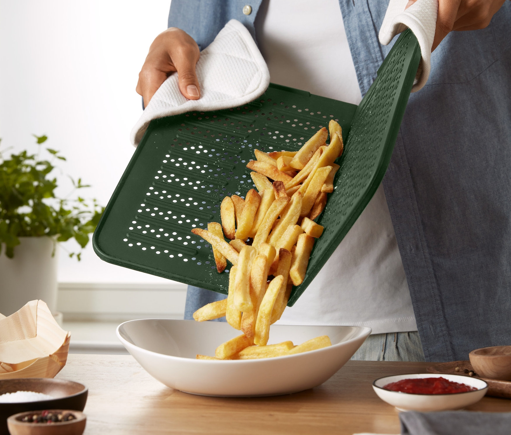 Osoba w rękawicy kuchennej przesypuje frytki z silikonowej blachy do pieczenia do miski.
